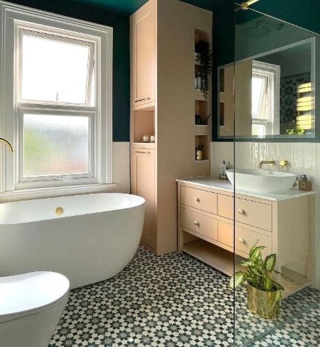 Bathroom with green star pattern floor tiles, white freestanding bath, pale pink cabinetry and a dark green wall