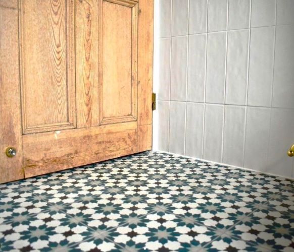 Green and white star pattern floor tiles laid beside an old timber door and white wall tiles