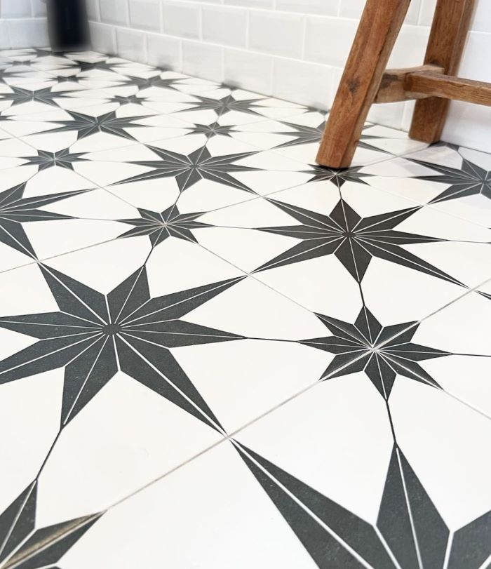 Close up of black and white star pattern floor tiles in a bathroom with white subway wall tiles and a timber stool
