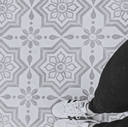 Grey and white star and flower pattern floor tiles seen from above with sneakers for scale