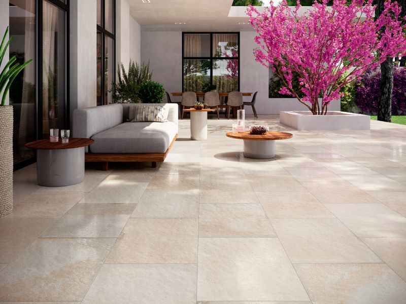 Pale stone look outdoor paving tiles on a terrace with lounge seating and a flowering tree